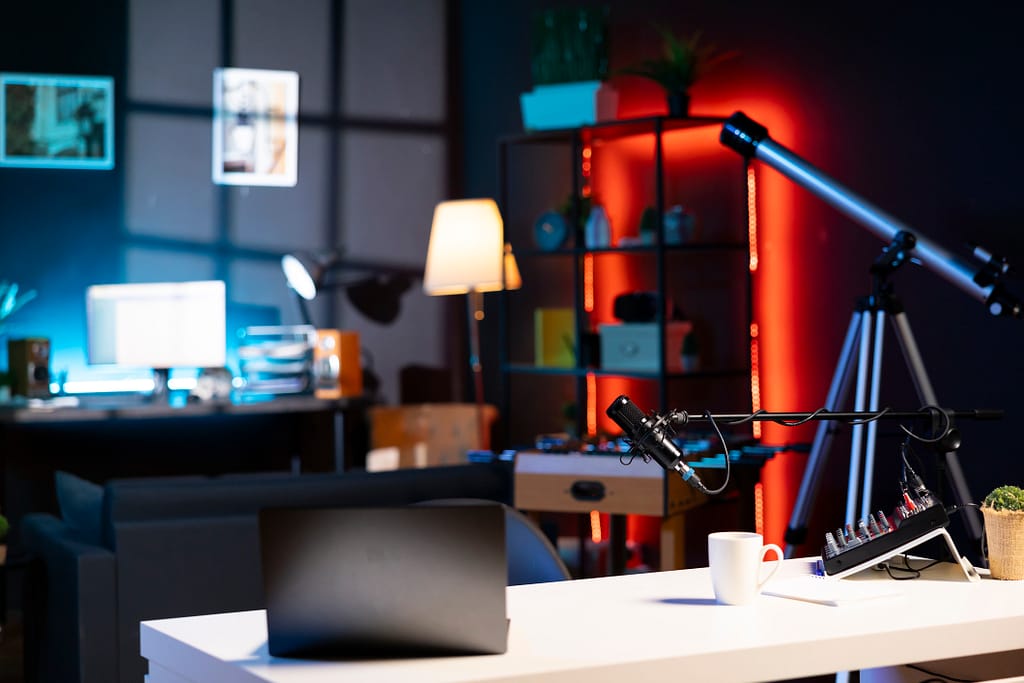 Internet video production gear in empty home studio interior illuminated with RGB lights at night. Professional microphone, sound mixer and other content creation equipment in apartment room