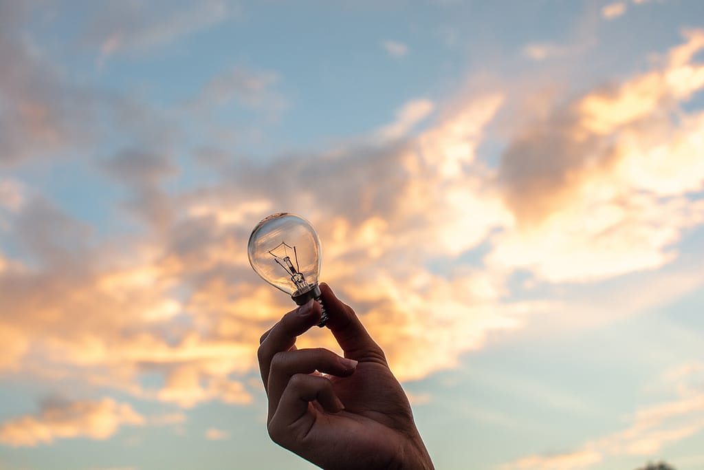 Hand holding a light bulb against a vibrant sunset sky, symbolizing creative ideas and strategic thinking for brand therapy at Fix & Form.