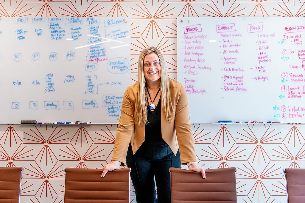 Smiling businesswoman standing in a modern conference room with whiteboards covered in marketing strategy notes, symbolizing planning, organization, and professional growth.